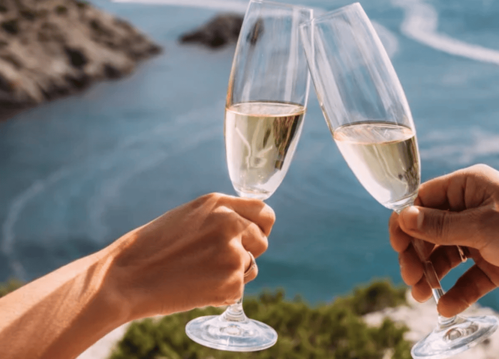 Two people toasting with champagne glasses against a scenic ocean backdrop.